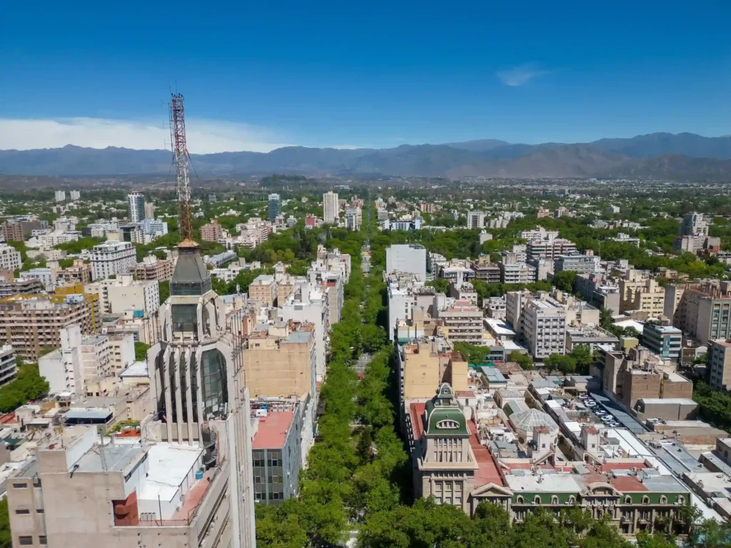 Vista aérea urbana da cidade de Mendoza com vinícolas ao redor e a Cordilheira dos Andes majestosa ao fundo.